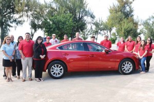 Triple J Motors general manager Randy Steele, center, in checkered shirt, together with Northern Marianas College president Dr. Carmen Fernandez, fifth from left, and NMC students, pose with the Mazda6i Sport that is featured as a hole-in-one prize in the upcoming NMC Foundation Golf Tournament on March 18. (NMC)