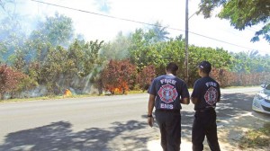 Two firefighters wait for a firetruck as a brush fire spreads along the side of the Tun Joaquin Doi Road in Chalan Kanoa Thursday afternoon. An off-duty firefighter who was passing by the area noticed the blaze and immediately called the Department of Fire and Emergency Medical Services. After a few minutes, firefighters and a small fire truck came and stopped the blaze from burning a power pole and destroying more vegetation. (Ferdie de la Torre)
