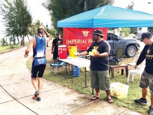 A team member from Imperial Pacific International Ltd.’s Corporate Social Responsibility hands out water to athletes along the pathway on Beach Road at the recently staged 2017 Tagaman Triathlon. (IMPERIAL PACIFIC)