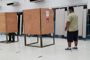 A Commonwealth Election Commission poll supervisor watches as a voter exercised his right to vote