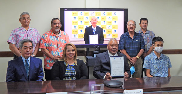 Katori City Mayor Seiichi Ui, on TV screen, and Saipan Mayor David M. Apatang, seated second from right, hold up the signed sister-city agreement between the Saipan and Katori City municipalities last Friday at the Saipan Mayor’s Office conference room.